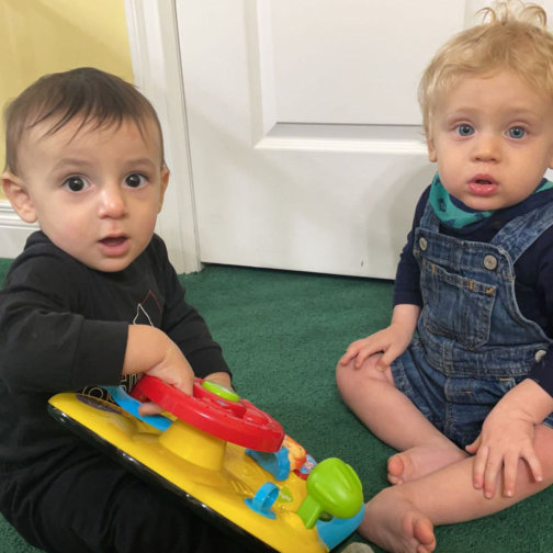 two babies playing with a toy stiring wheel